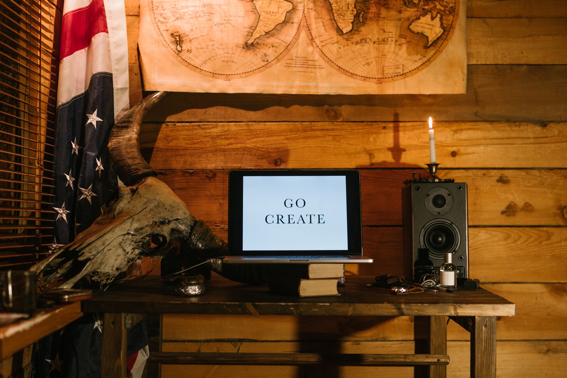 Rustic workspace featuring a laptop with 'Go Create', vintage map, and candlelight ambiance.
