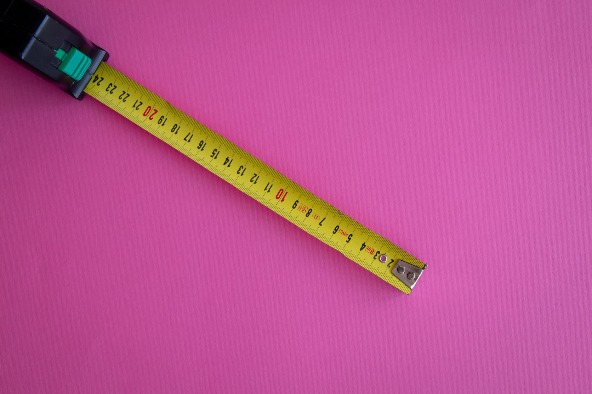 A yellow measuring tape extended on a vibrant pink background, offering ample copy space.