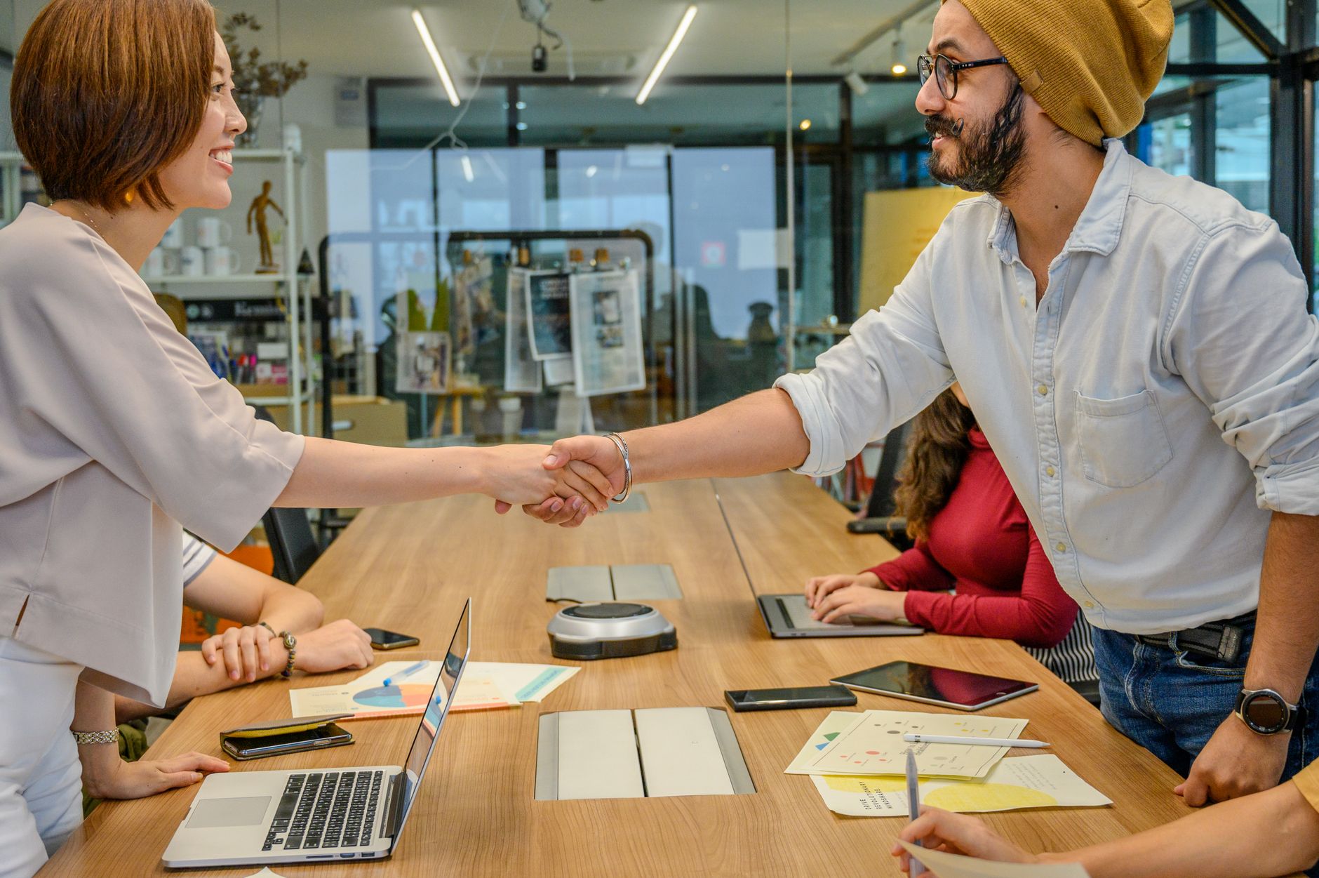 Diverse team in a modern office engaged in a collaborative meeting, sealing a partnership with a handshake.