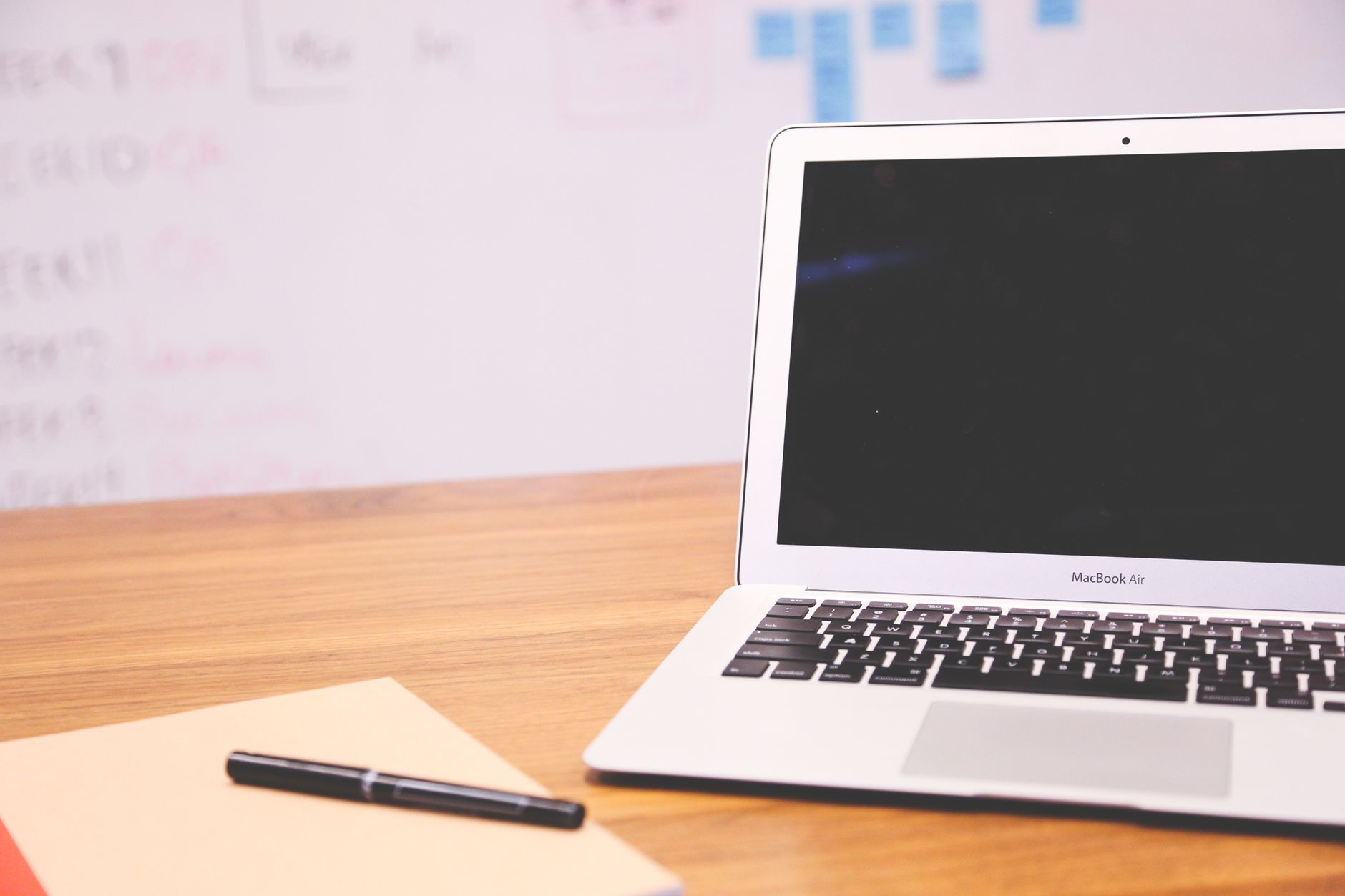 Sleek laptop on wooden desk with pen and notepad, ideal for business and tech settings.