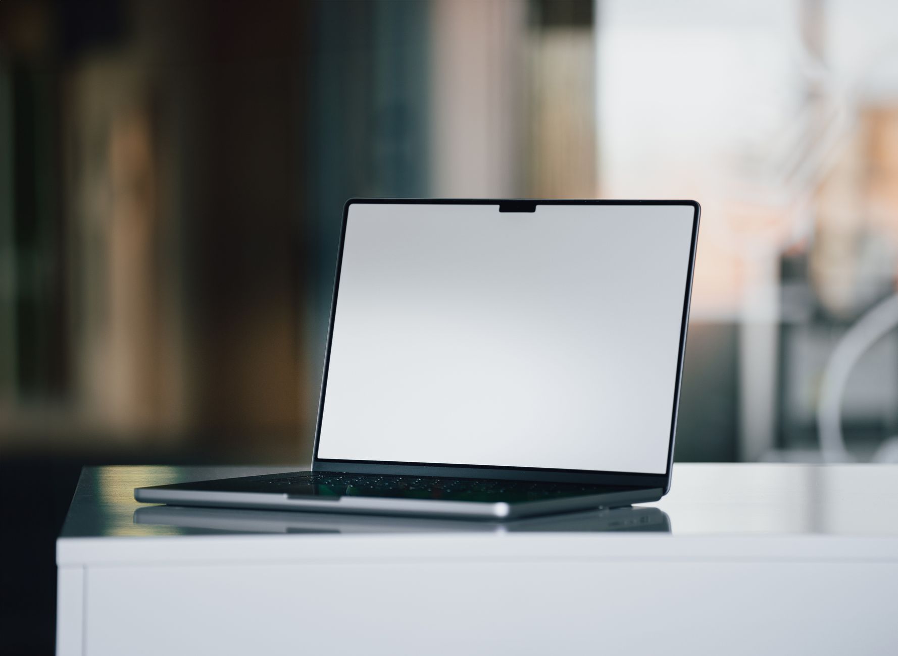 A sleek laptop with a blank screen sits on a white desk in a contemporary office setting.