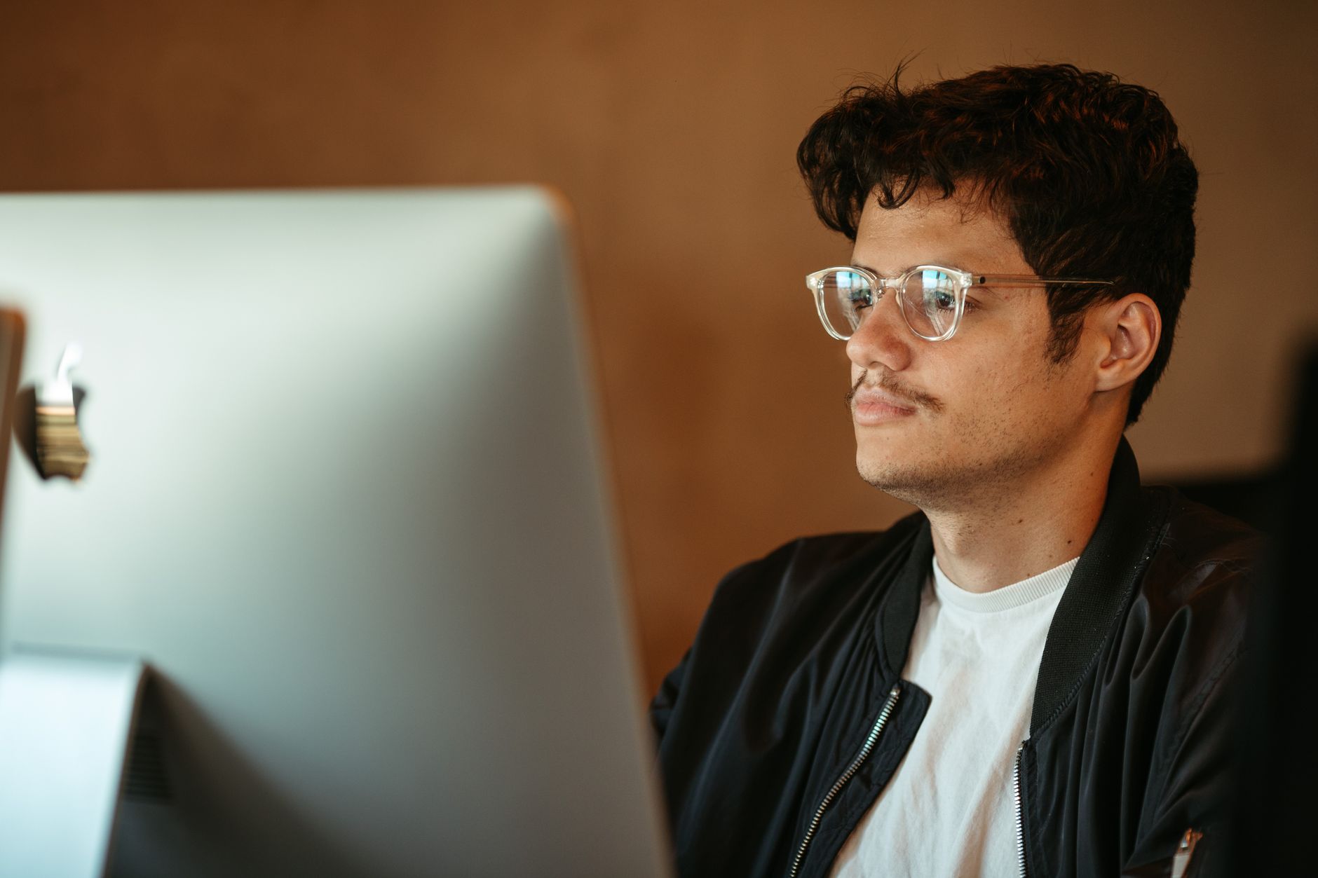 Young man in eyeglasses focusing on computer screen indoors.