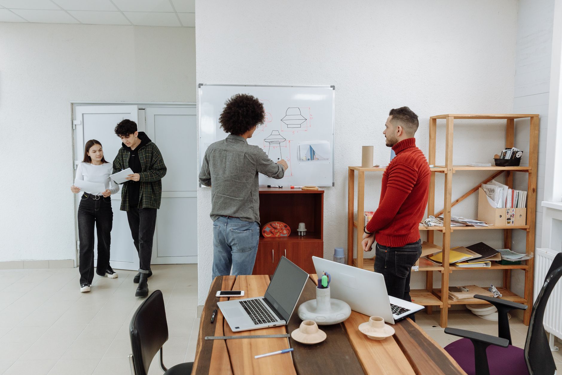 Diverse team collaborating in a modern office, discussing ideas with laptops and a whiteboard.