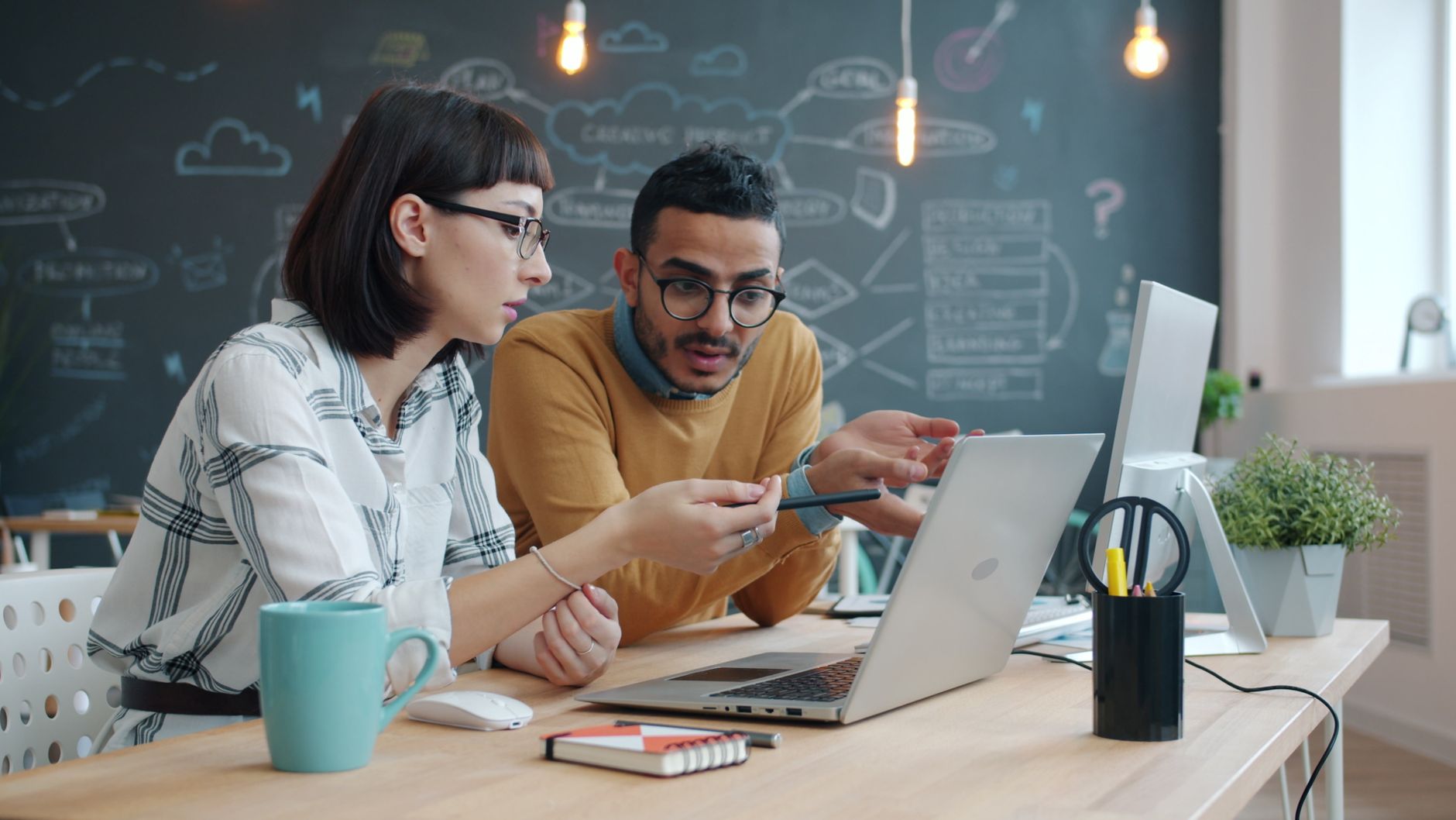 Two colleagues discussing work on a laptop in a creative office space.