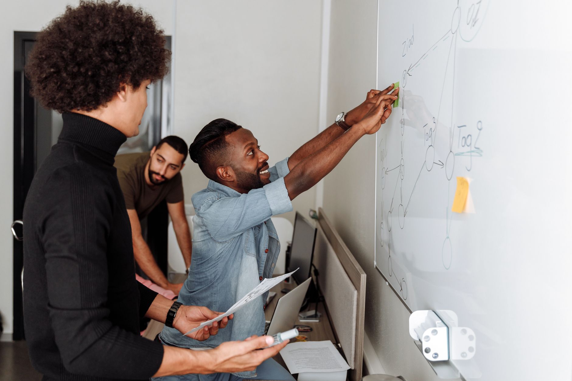 A diverse team of professionals brainstorming solutions at a whiteboard in an office setting.