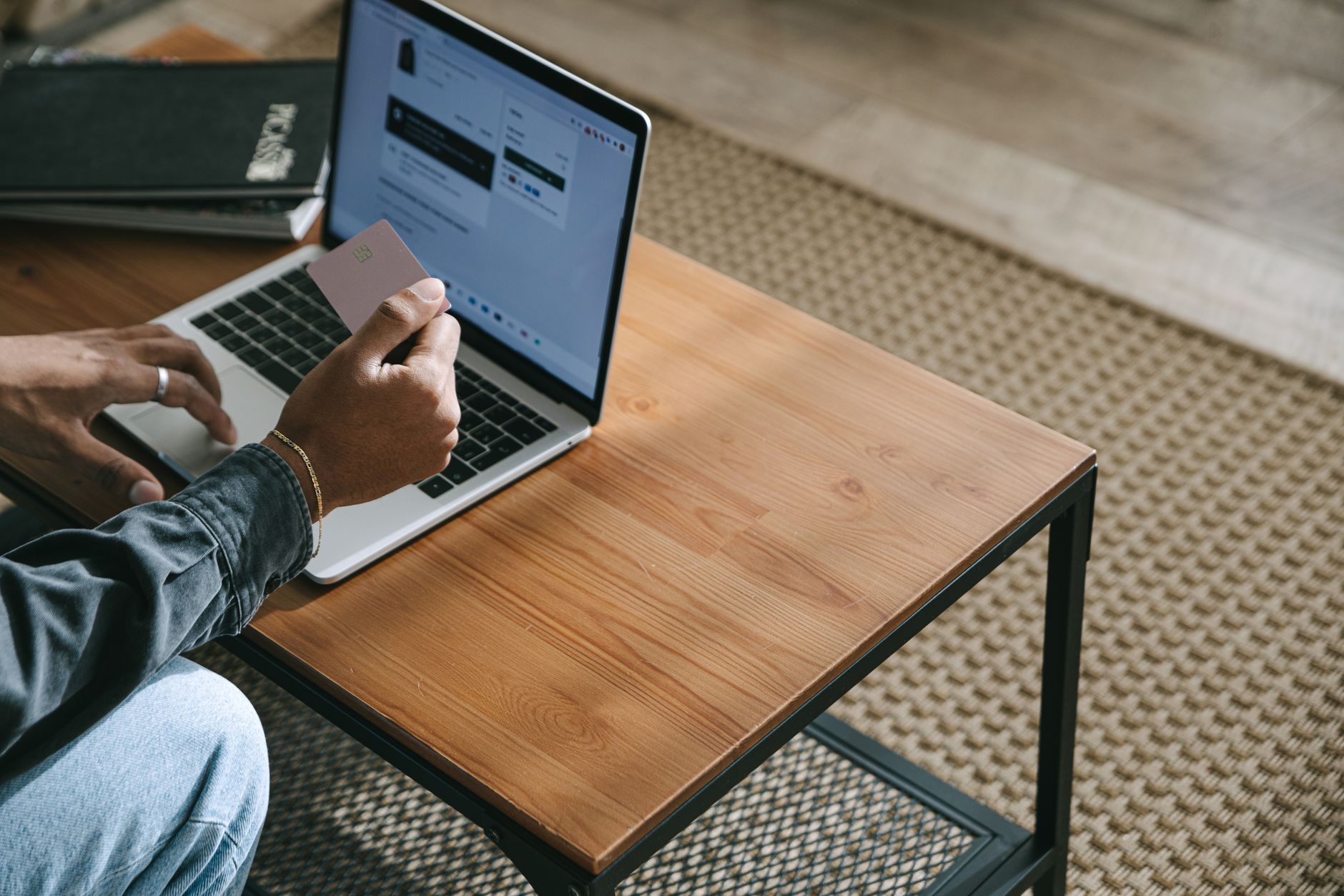 Person holding a credit card while shopping online using a laptop on a wooden table.