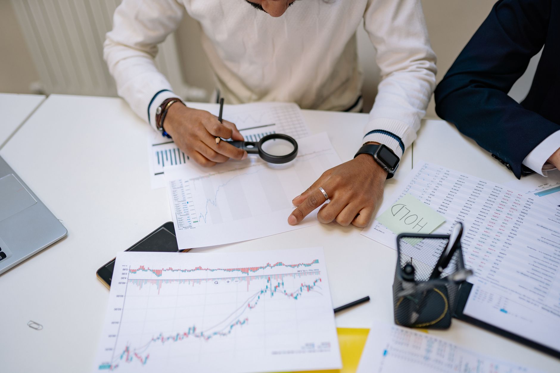 Business professionals reviewing charts with a magnifying glass in an office setting.