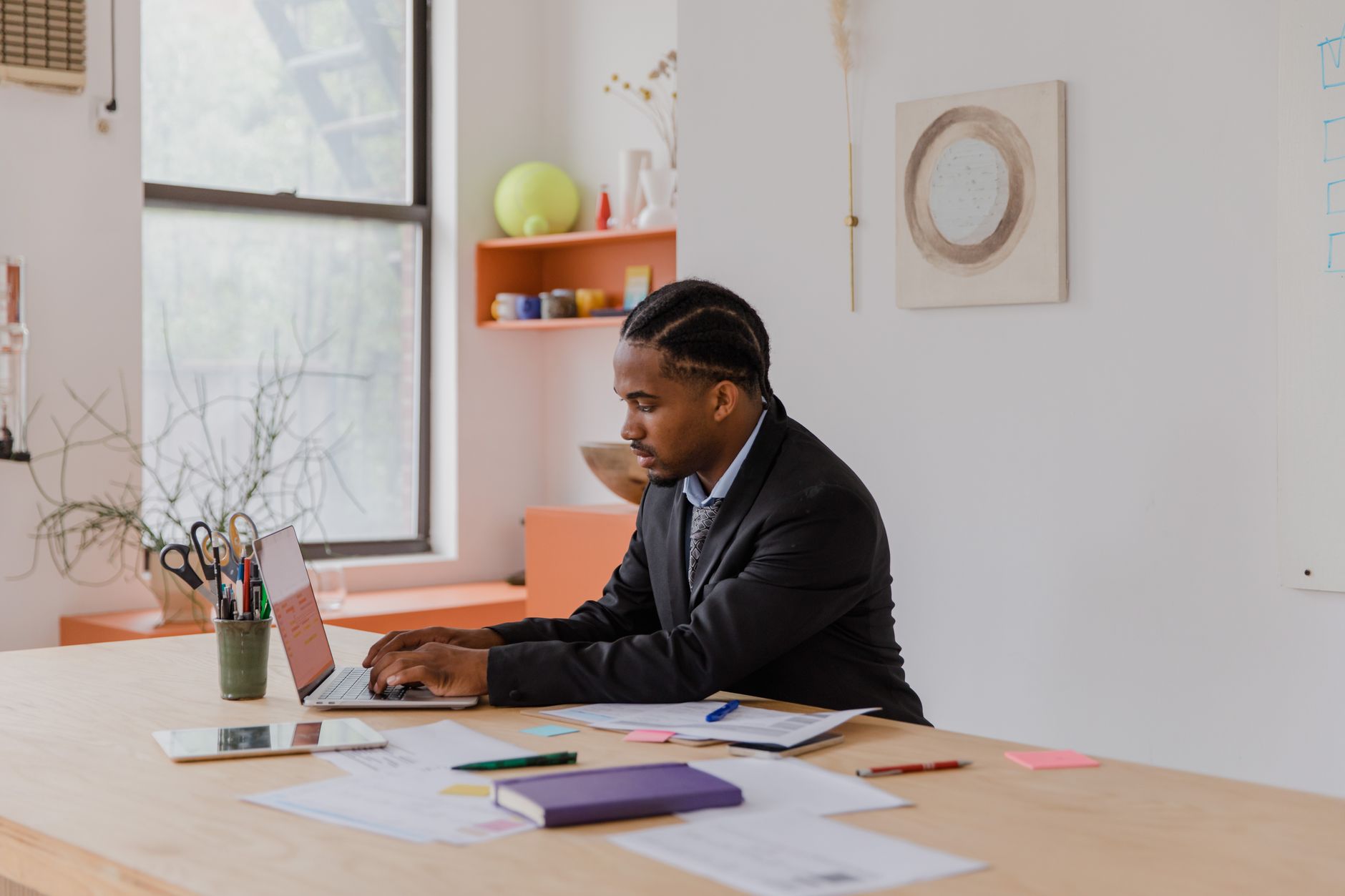 Professional businessman with braided hair working on a laptop at an office desk.
