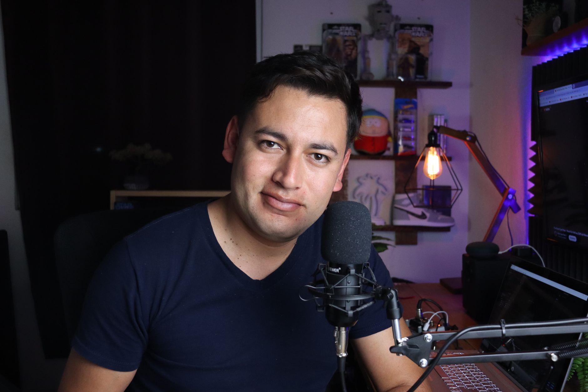 Podcaster in his home studio with microphone and laptop, creating digital content.