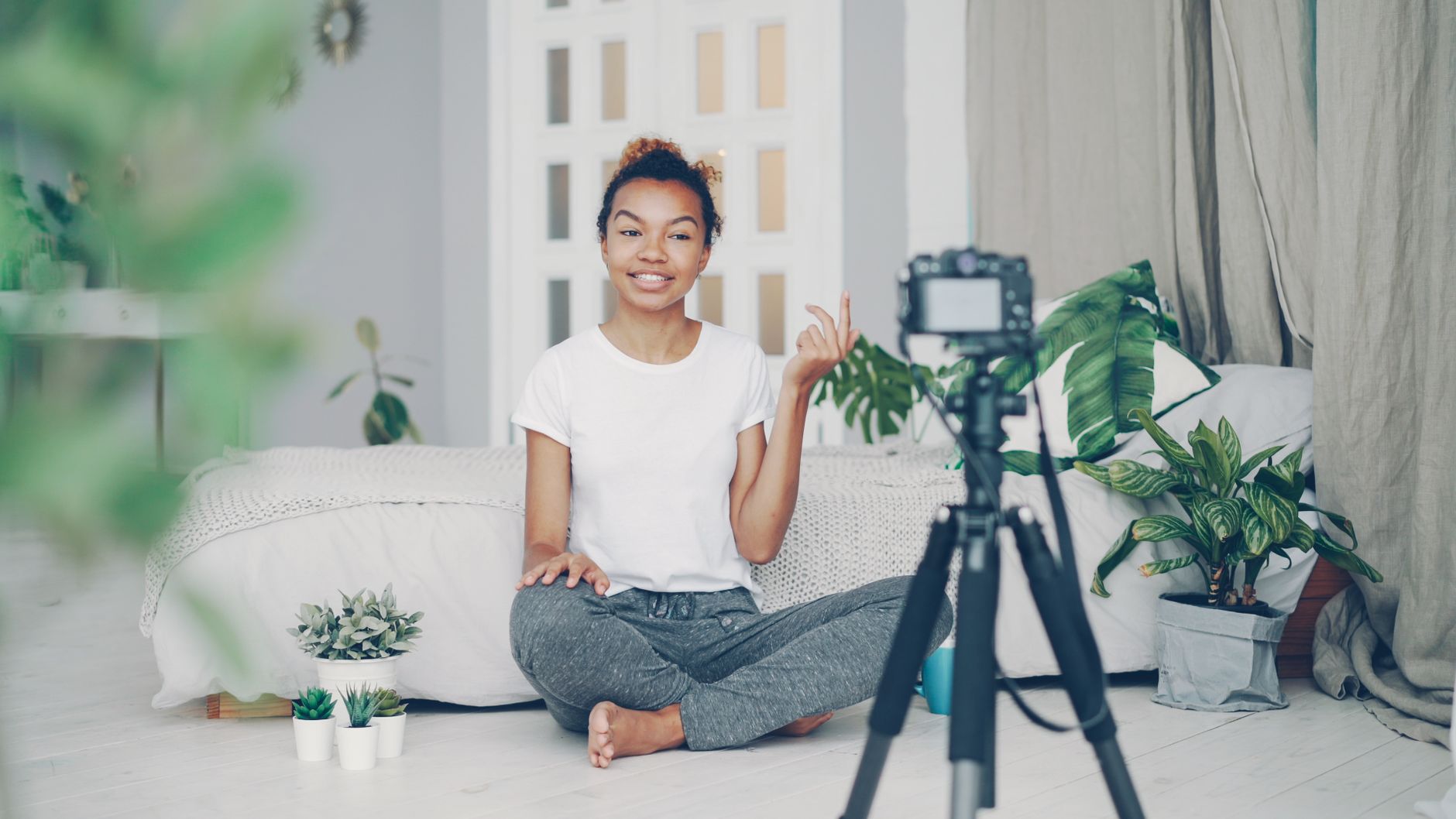 A woman vlogging indoors in a cozy setting with houseplants and decor.