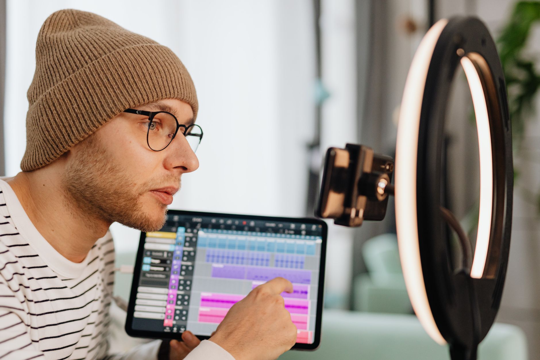 Man wearing glasses and beanie using a tablet with a ring light, indoors.