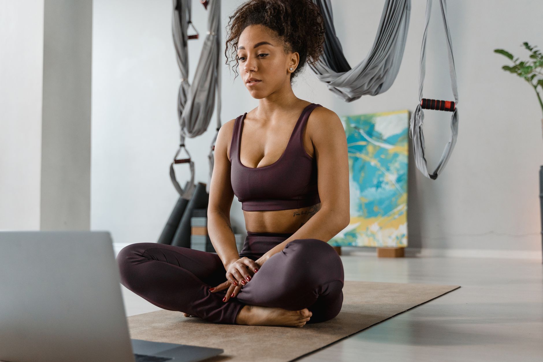 A woman in activewear practicing yoga indoors, sitting cross-legged with a laptop.