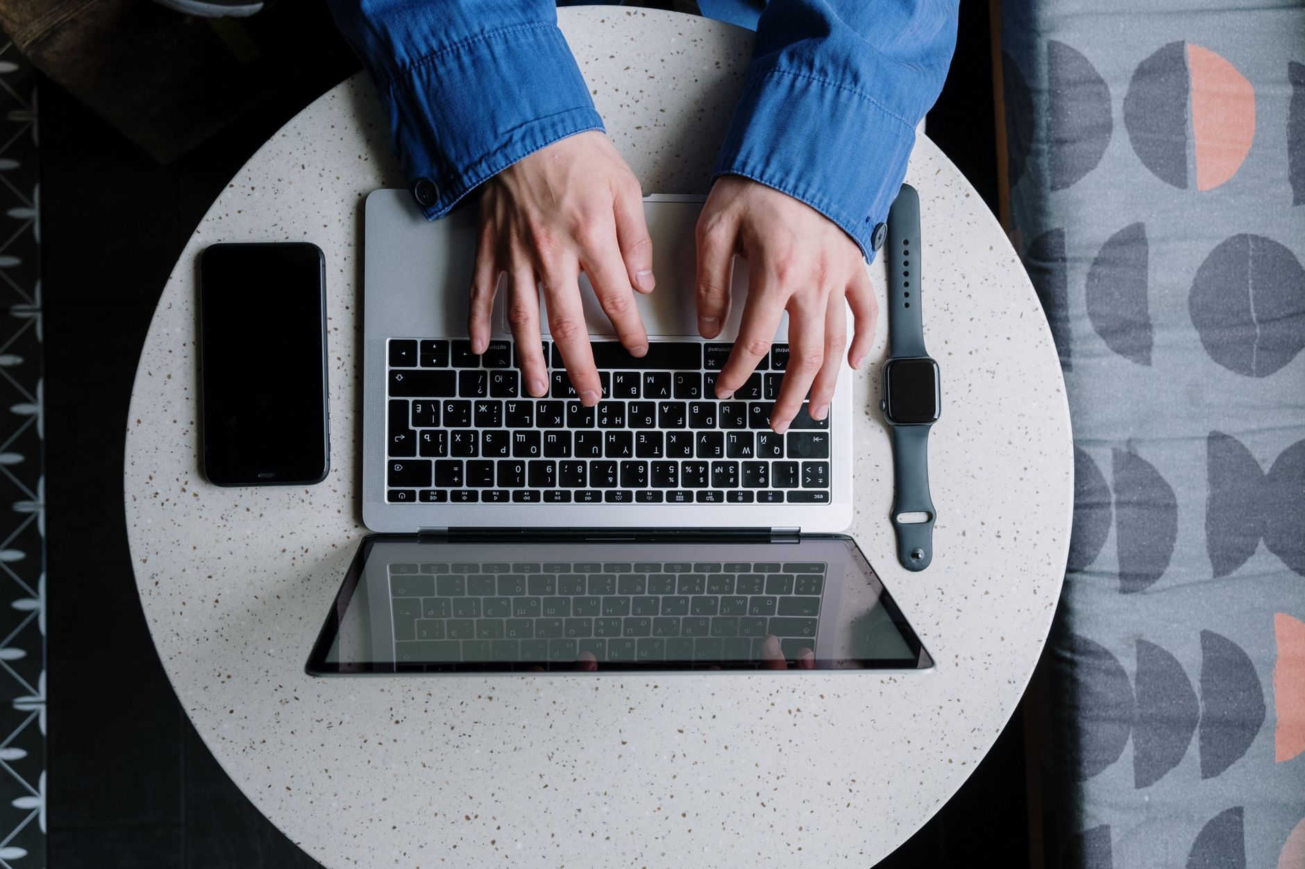 Casual setting with hands typing on a laptop, accompanied by a smartwatch and smartphone.