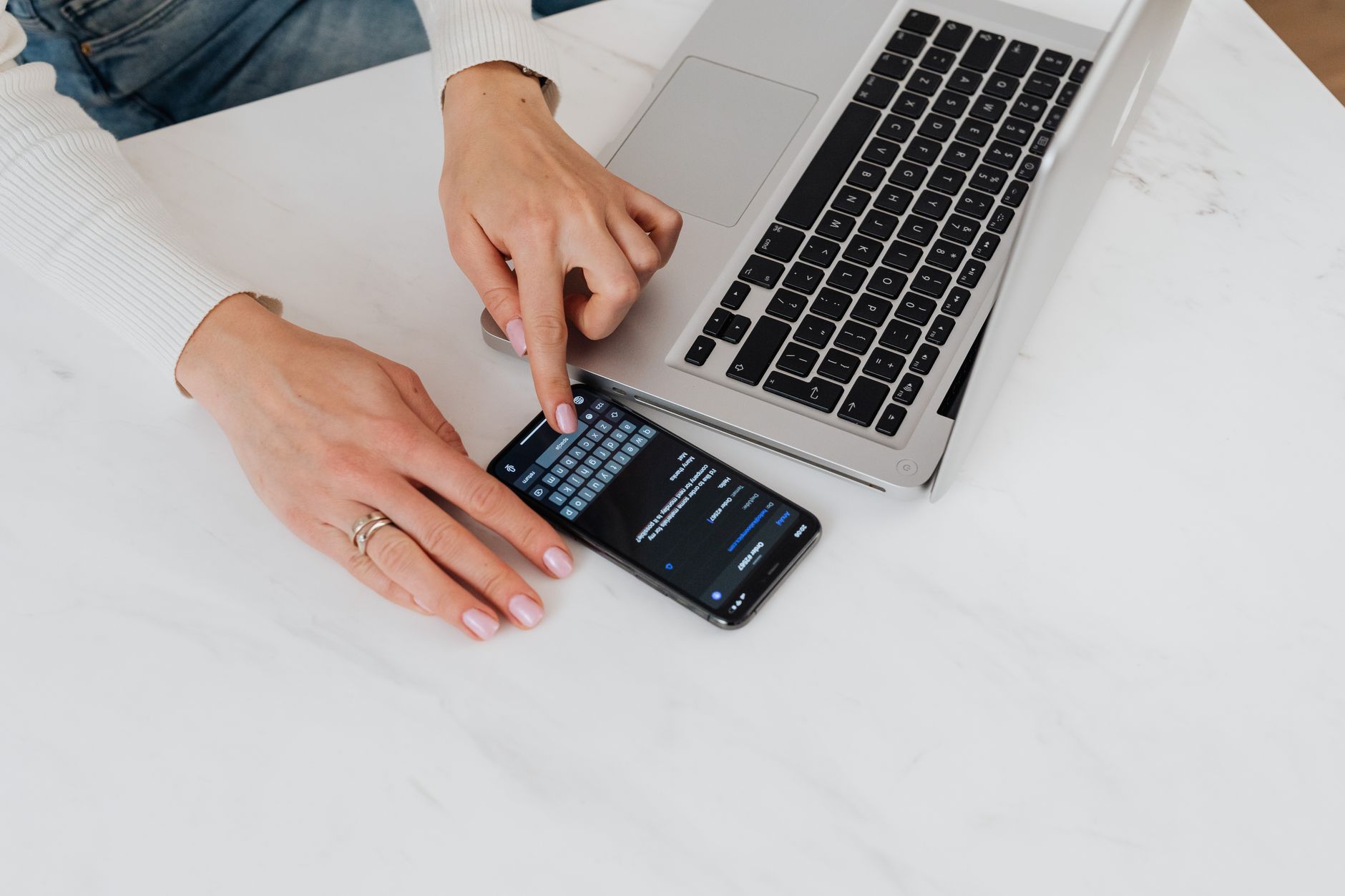 Close-up of hands using smartphone and laptop on a white desk. Perfect for tech and business concepts.