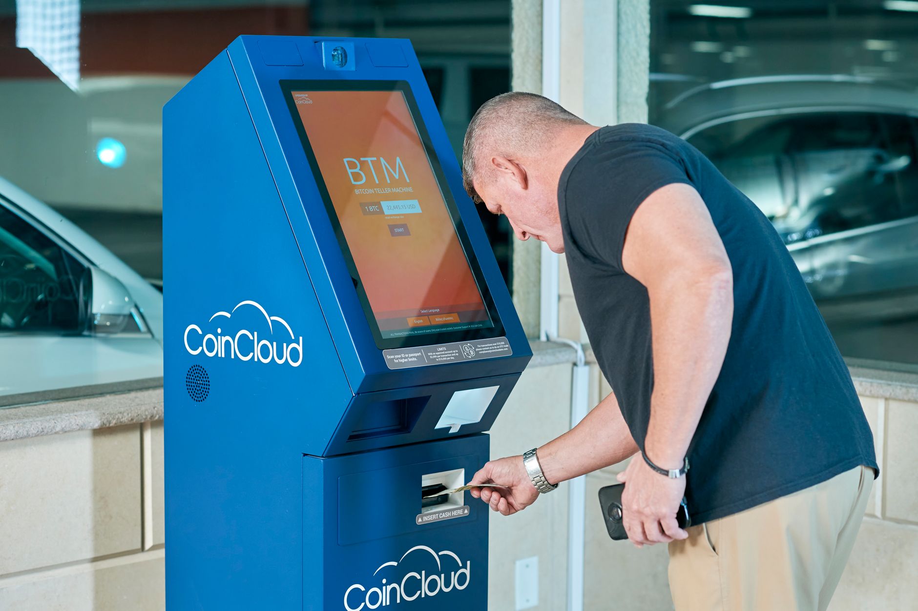 A man interacts with a CoinCloud Bitcoin ATM indoors, making a cryptocurrency transaction