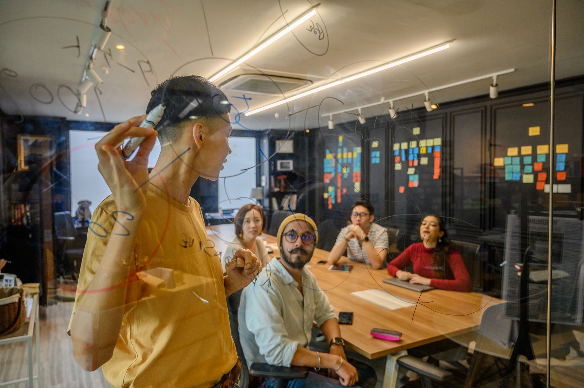 Group of professionals collaborating in an office, brainstorming on glass board.