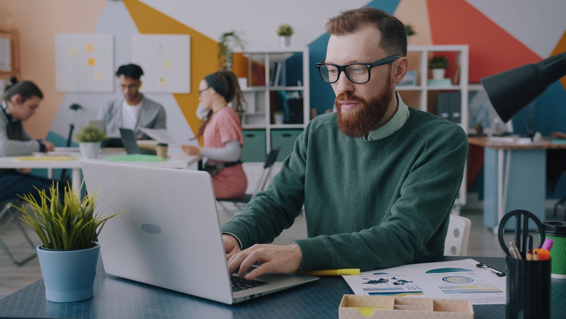 A team in a colorful modern office working collaboratively on laptops and documents.