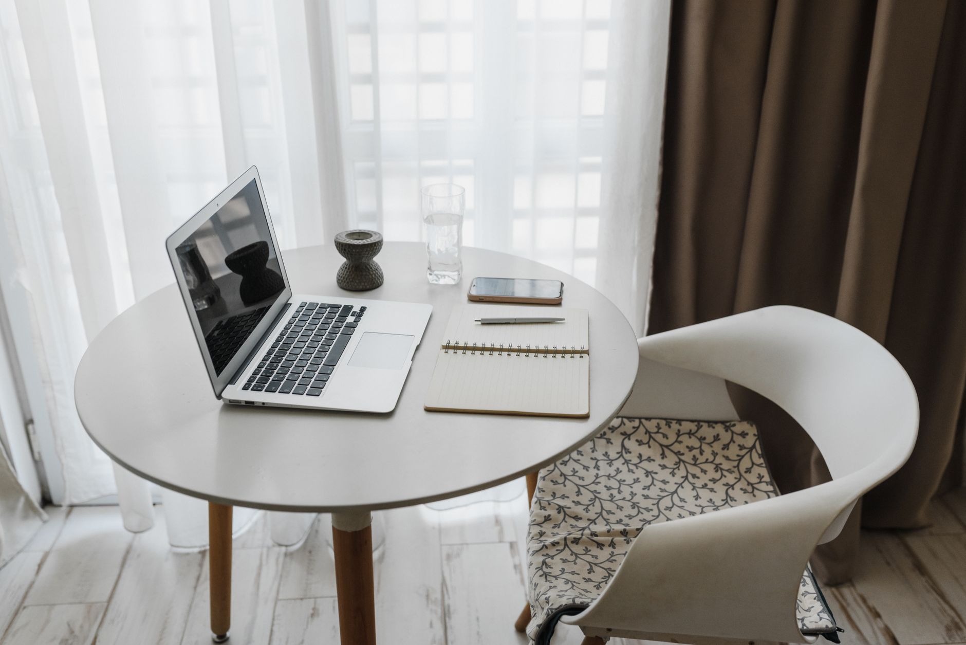 A stylish home office setup with a laptop, notebook, and smartphone on a round table.