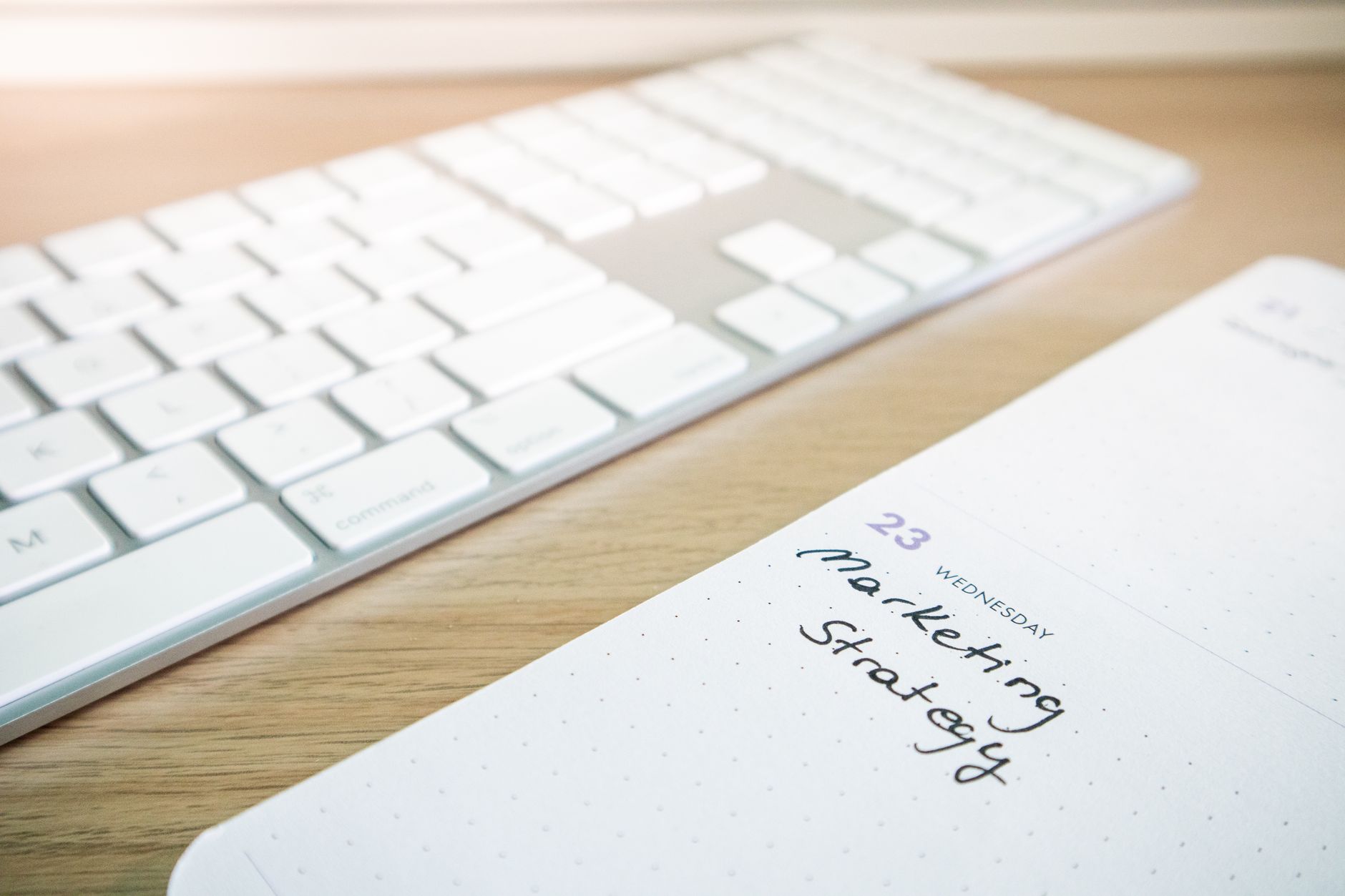 Notebook with marketing strategy note alongside a keyboard on a wooden desk.