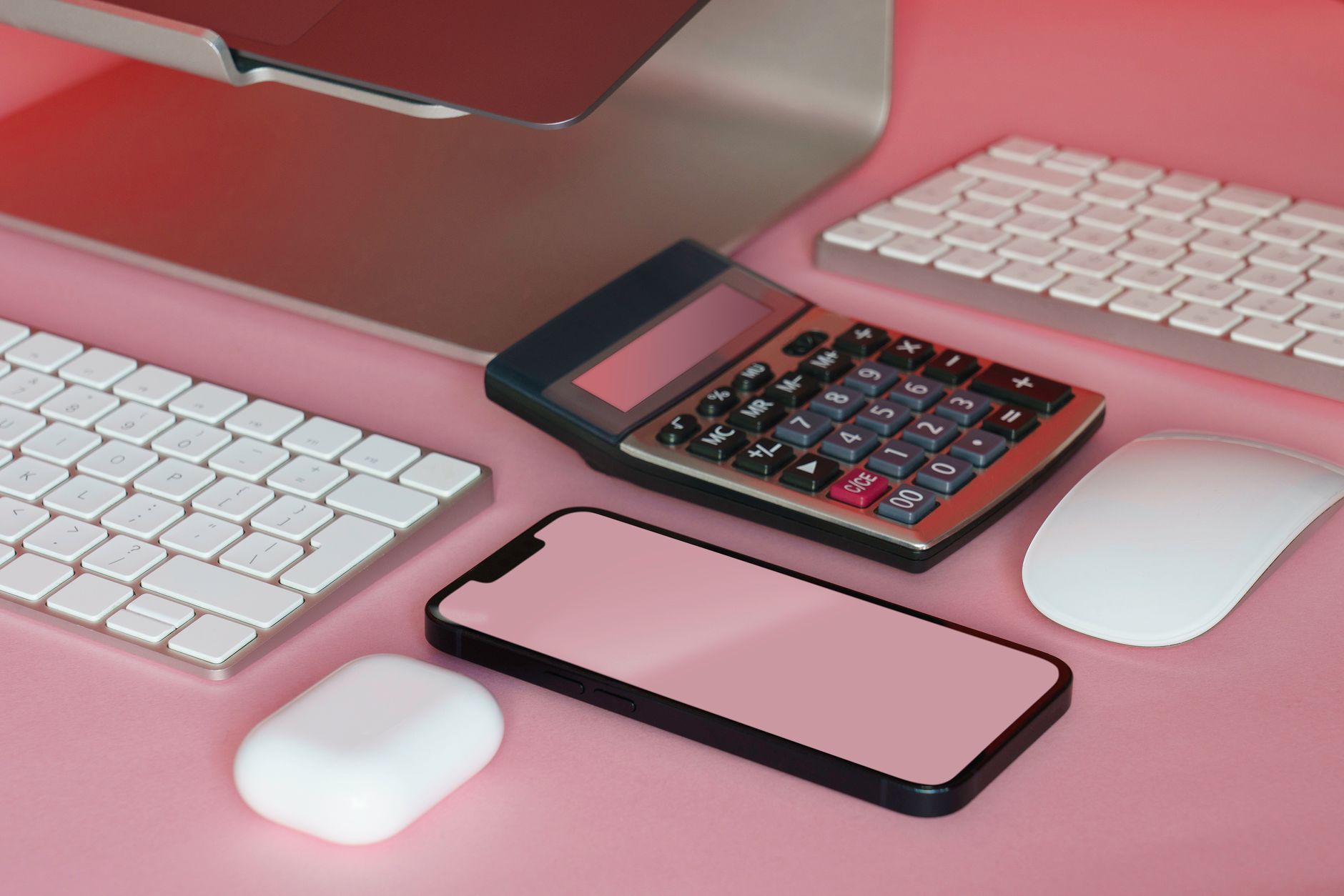 A stylish setup of office gadgets on a pink surface, including a smartphone and calculator.