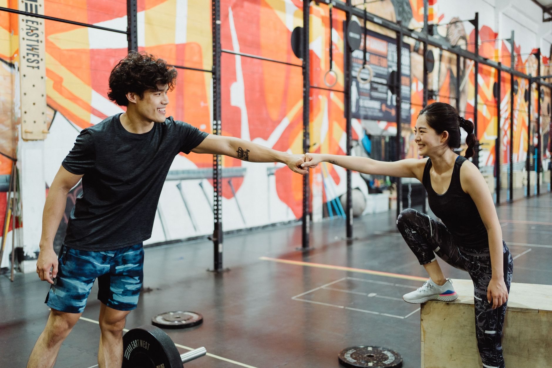 Active couple in sportswear fist bumping during a workout session in a vibrant gym.