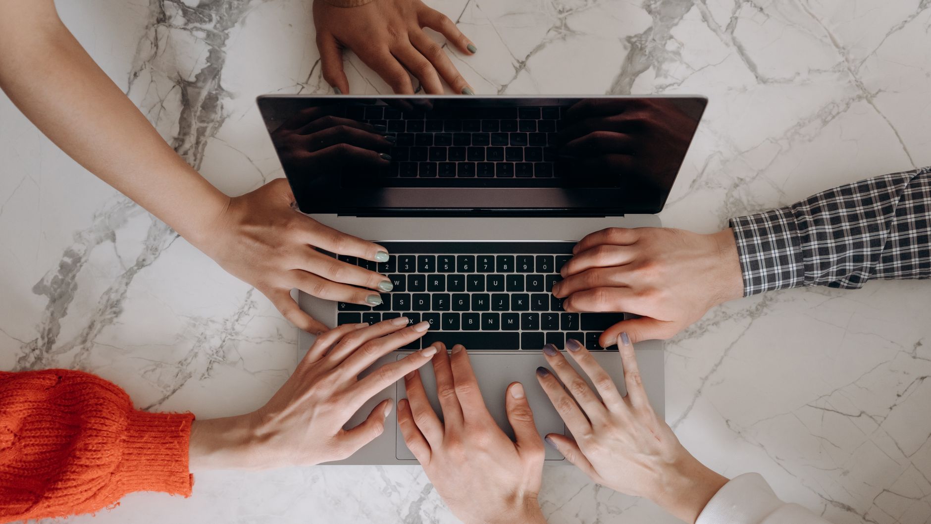 Top view of multiple hands working together on a laptop keyboard, symbolizing teamwork.