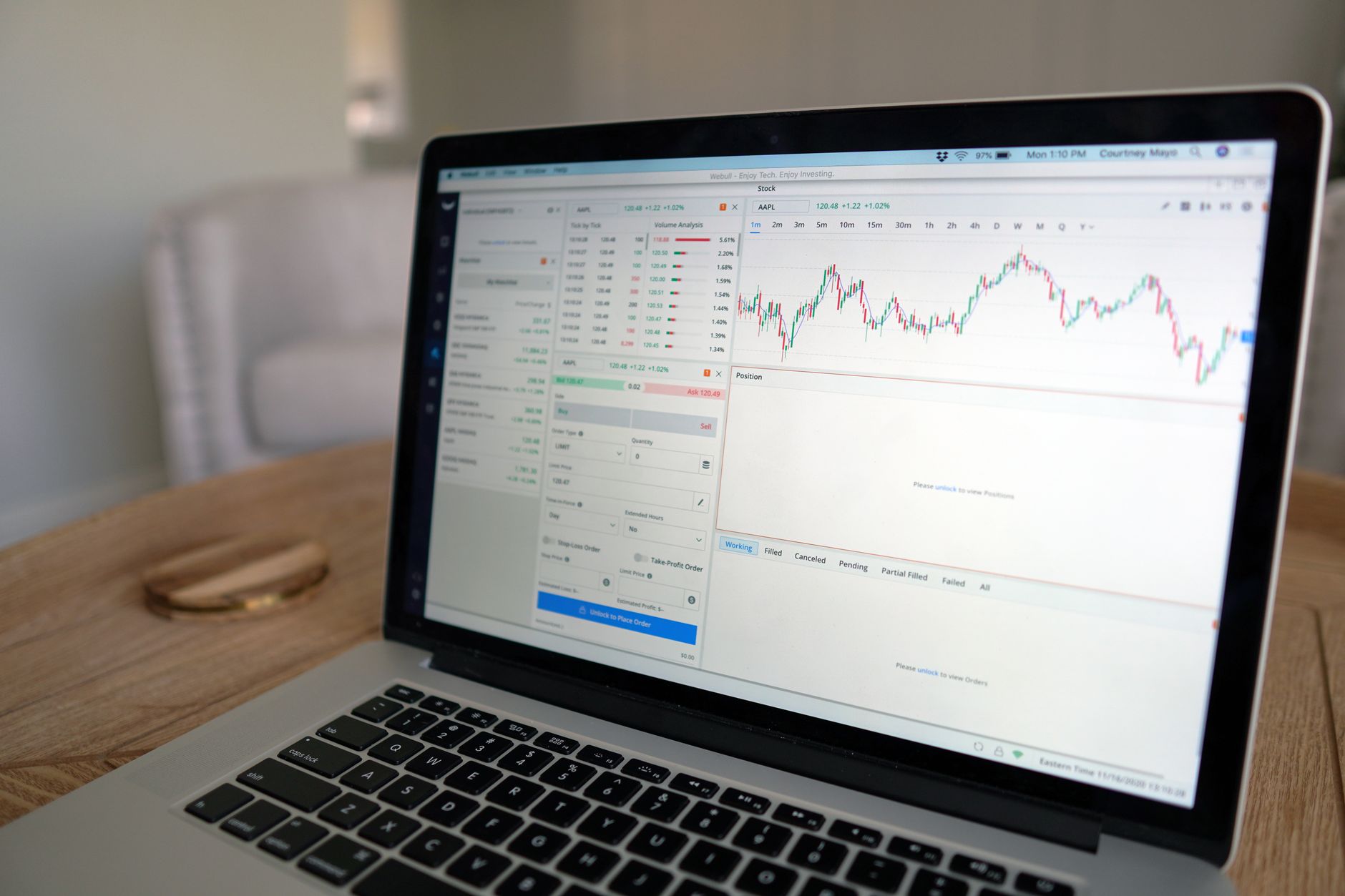 Close-up of a laptop displaying stock trading software with a market chart on a wooden table.